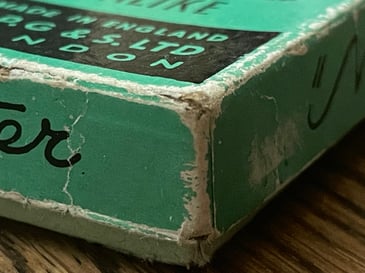 The corner of a green, vintage card box. The edges are distressed with age.