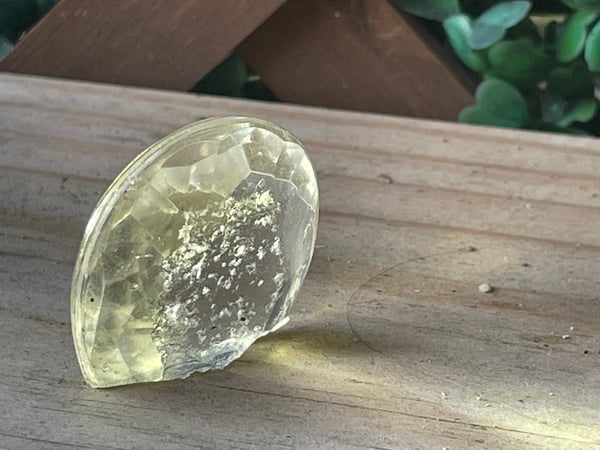 Photo of a broken chandelier crystal. One end is missing, and there are scratches and pits in the glass. Light is shining through the crystal.